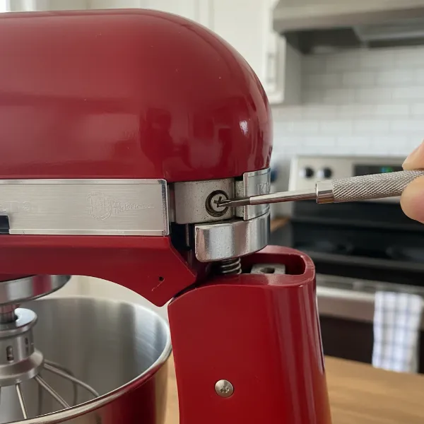 A close-up of a stand mixer's adjustment screw for beater-to-bowl clearance calibration.